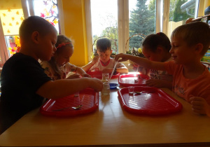 Dzieci siedzą przy stoliku, w ręce trzymają pipetki, które napełniają wodą i przelewają do pojemników z drożdżami.
